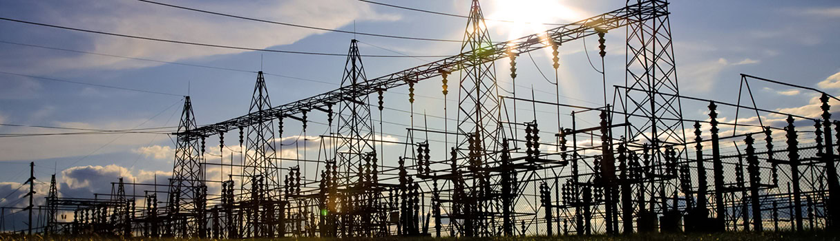 Sunset behind an extensive electrical substation with multiple high-voltage towers and power lines, illustrating the energy industry.