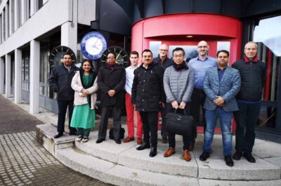 Delegación de altos cargos del Metro de Dhaka en Sumiswald con miembros del equipo MOBATIME delante del edificio MOBATIME, relojes analógicos detrás a la izquierda